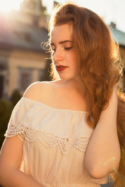 Portrait de rue de jolie fille rousse avec de longs cheveux ondulés posant dans l'éblouissement du soleil
 - Photo, image