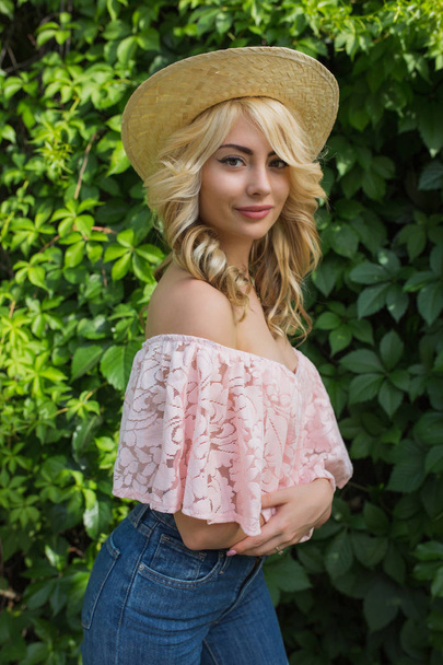 Pretty young woman with lush wavy hair wearing hat and stylish outfit posing near the vine - Foto, Imagem