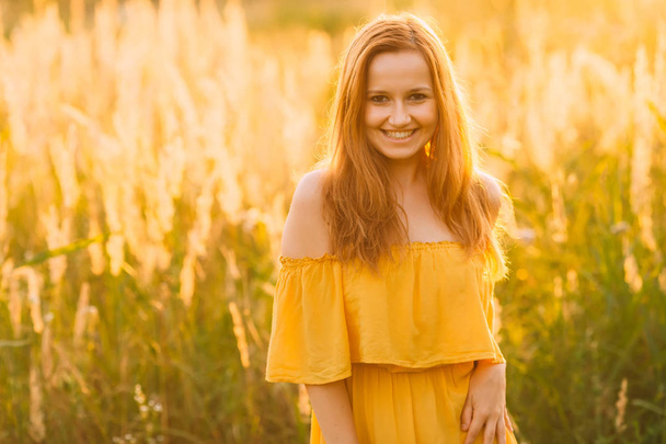 a beautiful girl in a stylish dress laughing and looking into the camera lens on a field with high grass - Zdjęcie, obraz