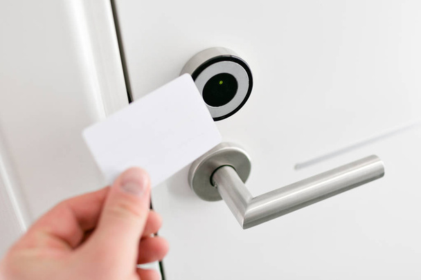 Hoteldeur - jonge man met een keycard voor de elektronische sensor van een deur van de kamer. Concept vakantie of zakenreis - Foto, afbeelding