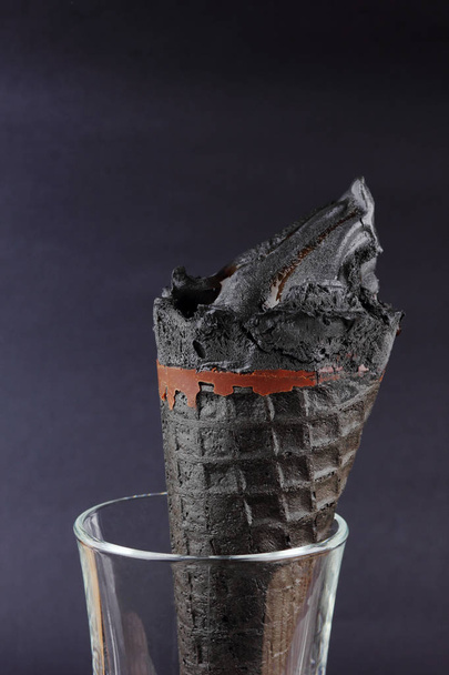 Black ice on a black background, ice cream with chocolate in waffle cone, stylish summer dessert, cold milk product for the designer, creative, copy space - Foto, afbeelding