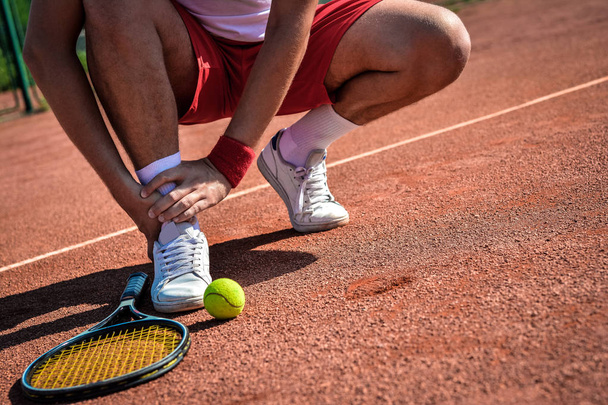 Sports injury. Close-up of tennis player touching his leg while sitting on the tennis court - Fotó, kép