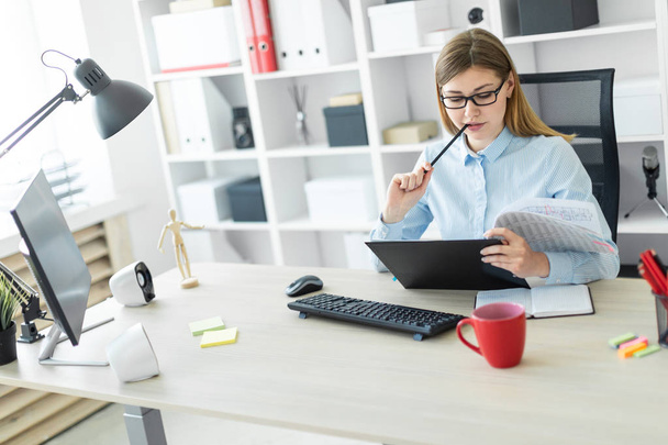 Mladá dívka v brýlích sedí za stolem v kanceláři, drží tužku v ruce a pracuje s dokumenty. - Fotografie, Obrázek