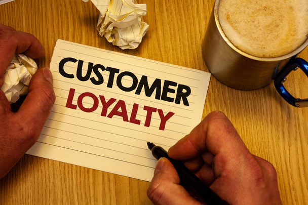 Handwriting text writing Customer Loyalty. Concept meaning Client Satisfaction Long-Term relation Confidence Man holding pen ideas notebook crumpled papers coffee cup wooden background - Photo, Image