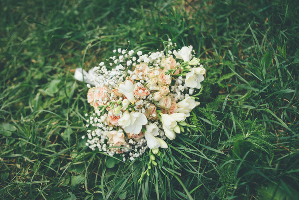 buquê de casamento com rosas e flores bege branco deitado na grama verde
 - Foto, Imagem