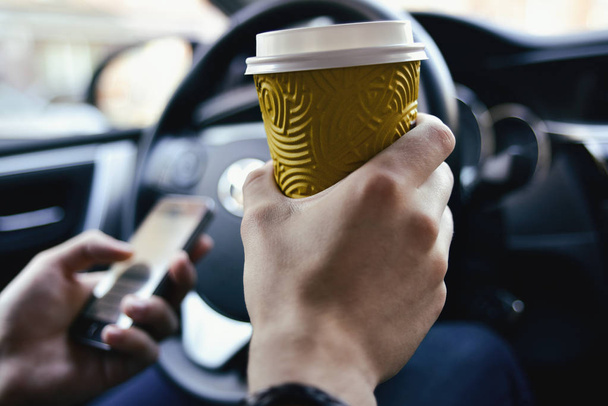 Los brazos del hombre sostienen un café y un timón en automóvil
 - Foto, Imagen