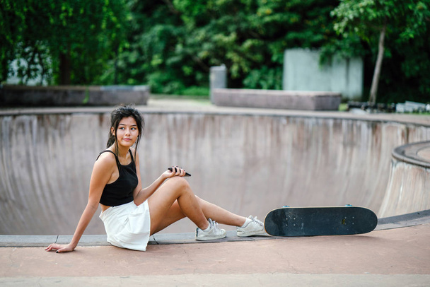 Portrait of Asian Chinese girl with mobile phone and skate in skatepark - Foto, Imagem