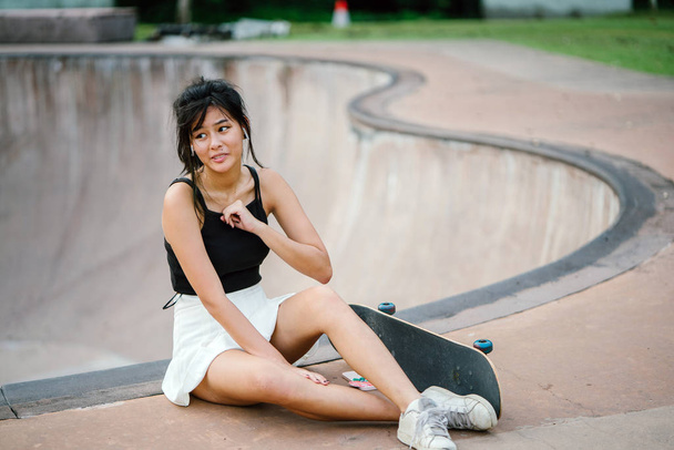 Portrait of Asian Chinese girl with mobile phone and skate in skatepark - 写真・画像