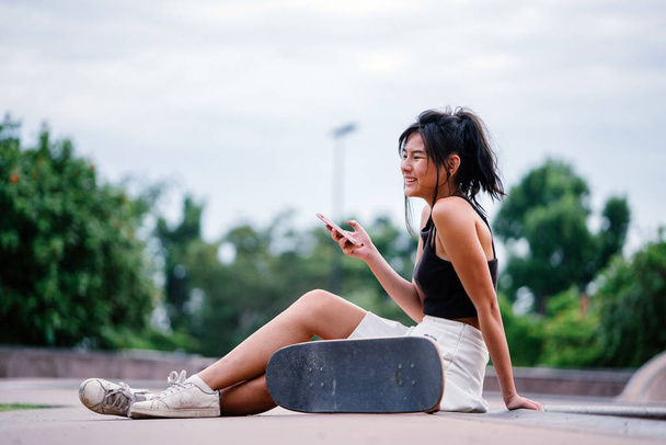 Portrait of Asian Chinese girl with mobile phone and skate in skatepark - Photo, image