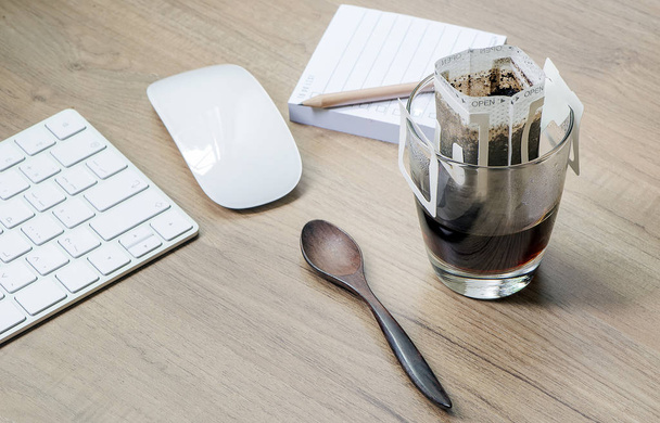 Миттєва свіжозварена чашка кави або паперовий мішок на чашці на дерев'яному столі з комп'ютерною клавіатурою та мишкою
 - Фото, зображення