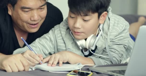 Asiático padre ayuda a su joven hijo mientras el niño está haciendo su tarea en casa
 - Imágenes, Vídeo