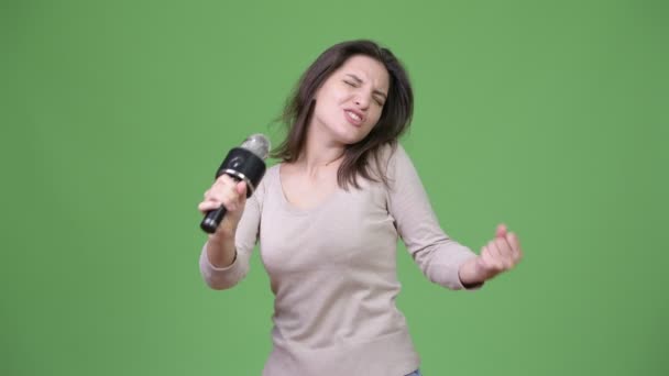 Young beautiful woman singing against green background - Imágenes, Vídeo