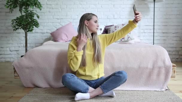 Iloinen houkutteleva nuori nainen ottaa selfie matkapuhelimella kotona
 - Materiaali, video