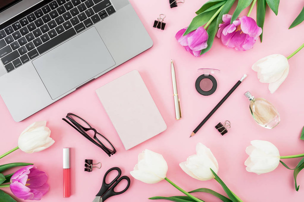 Escritório com laptop, flores de tulipa, cosméticos, óculos, diário e caneta sobre fundo rosa. Deitado. Vista superior
. - Foto, Imagem