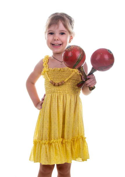Bambina con un vestito giallo brillante che tiene le maracas tra le mani. Studio foto, sfondo bianco brillante
. - Foto, immagini