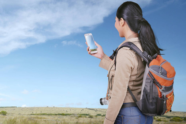 Jovem asiático turista mulher olhando para fotos em seu telefone inteligente no prado
 - Foto, Imagem