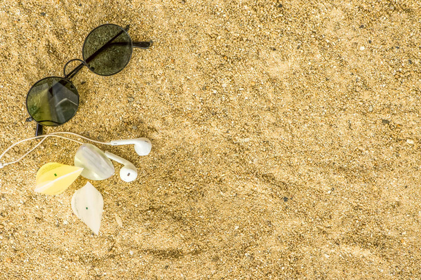 Gafas de sol negras, auriculares, crema de ducha, champú y loción, poner en la arena en la playa, con sol de la mañana, Vista superior
 - Foto, imagen