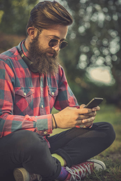 Fiatal férfi városi nézni használ mozgatható telefon. fiatal férfi textil-a cellphone - Fotó, kép