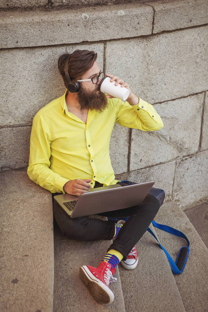 Homem jovem hipster trabalhando no laptop enquanto sentado nas escadas
. - Foto, Imagem