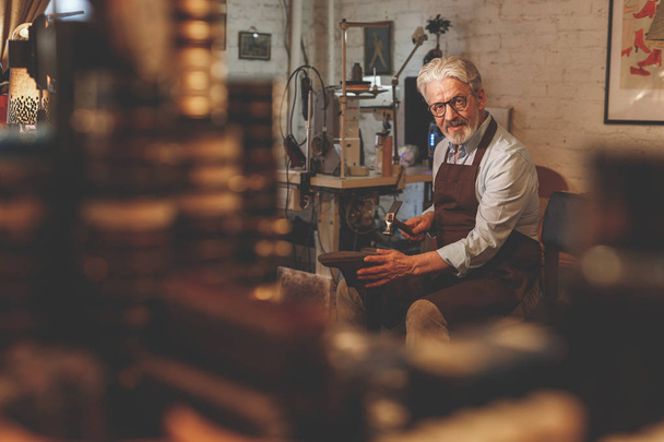 ein älterer Schuhmacher arbeitet in einem Atelier - Foto, Bild