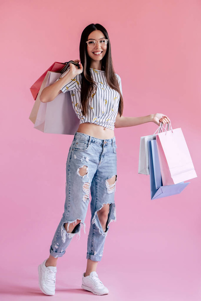 Asian teenage girl on pink background. Stylish young woman with shopping bags in hands - Foto, Bild