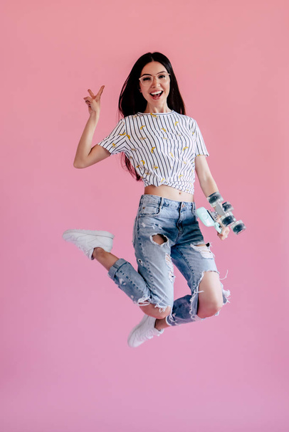Young asian teenage girl on pink background. Stylish young woman with skateboard isolated. - Fotó, kép