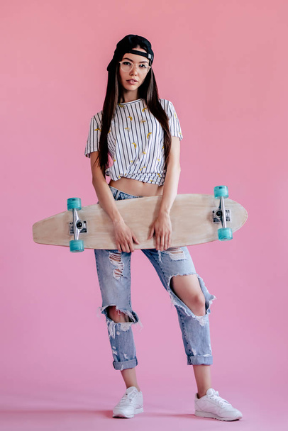 Young asian teenage girl on pink background. Stylish young woman with skateboard isolated. - Valokuva, kuva