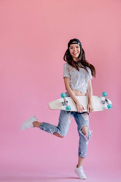 Young asian teenage girl on pink background. Stylish young woman with skateboard isolated. - Foto, afbeelding