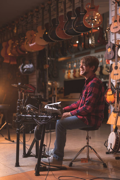 Smiling young man playing the drums in a music store - Photo, Image