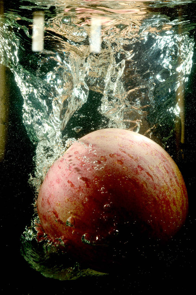 A red apple in a stream of water.A red apple in a stream of water and air on the black background. Water splashes from the falling Apple in the water. Red Apple in water. Fruit in water flow. - Foto, immagini