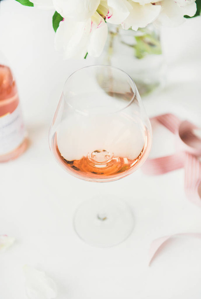 Rose wine in glass, pink decorative ribbon, peony flowers over white background - Fotoğraf, Görsel