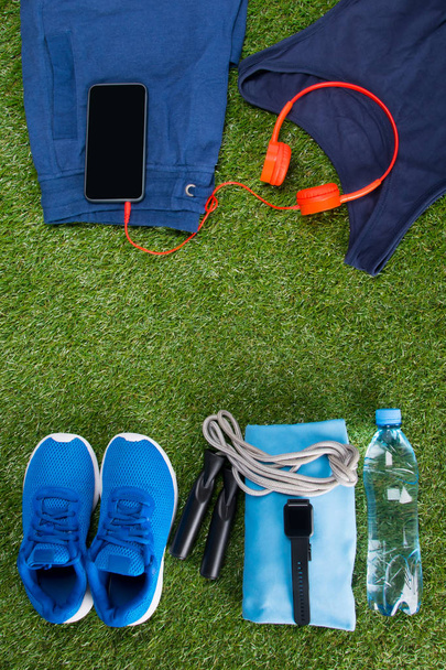 青いスポーツウェア、ボトル入り飲料水と草の背景にフィットネス用アクセサリー - 写真・画像