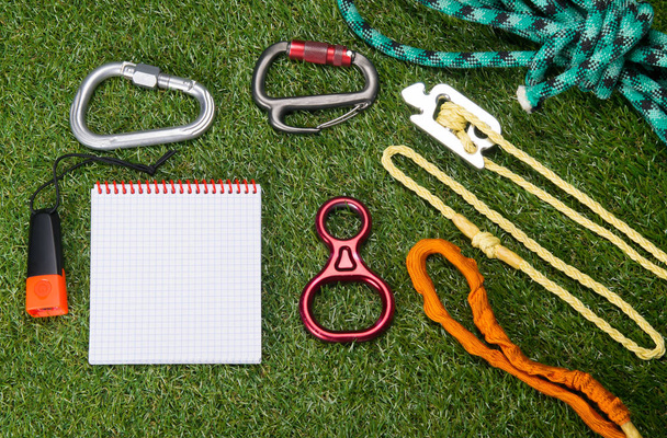 the subject of the insurance climber and a tourist kit are on the green background of the lawn. and there is a place to write on a light white notebook sheet - Фото, изображение