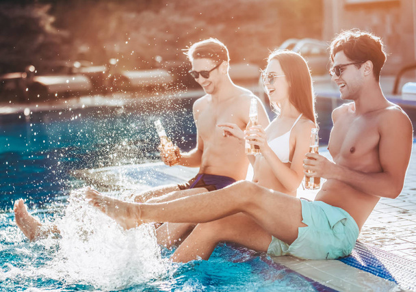 Group of young friends is having fun near swimming pool together, drinking beer and smiling. - Foto, Bild