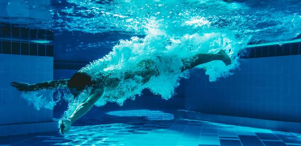 Man is jumping into the swimming pool. Man is swimming under water in swimming pool. - Foto, Imagem
