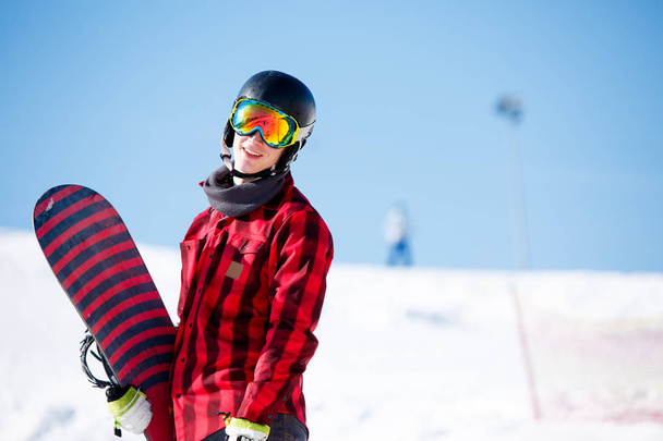 Photo of smiling man in helmet with snowboard on background of snowy hills - Foto, immagini
