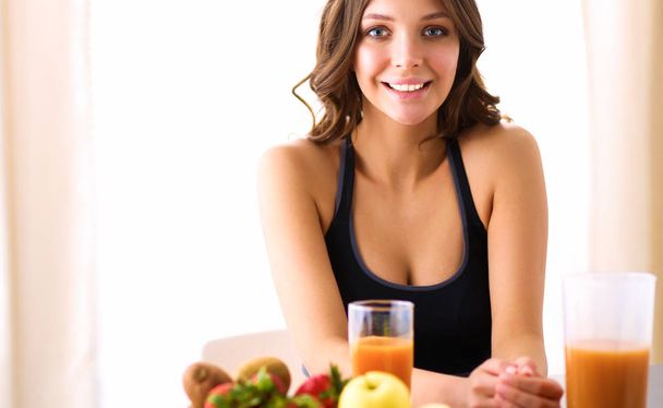 Girl sitting in the kitchen on the desk with fruit and glasses with juice - Фото, зображення