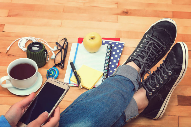 Женская рука с мобильным телефоном, ноутбуки, ручка, очки, музыкальные колонки, наушники, чашка чая, яблоко на деревянном фоне
 - Фото, изображение