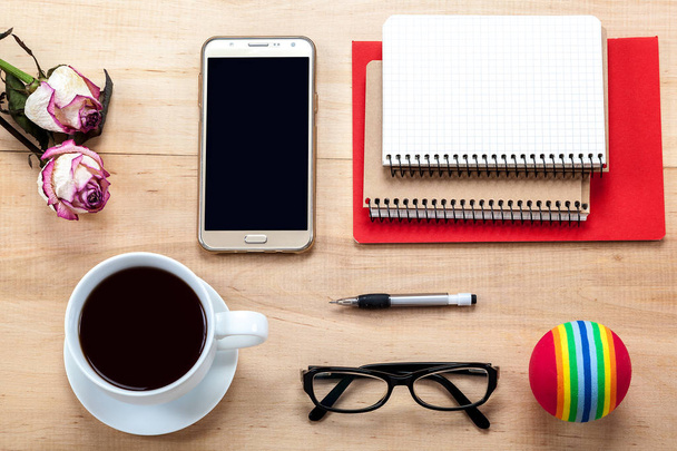 Mobile phone, glasses, a cup of tea, flowers, stationery on wooden background. - Photo, Image