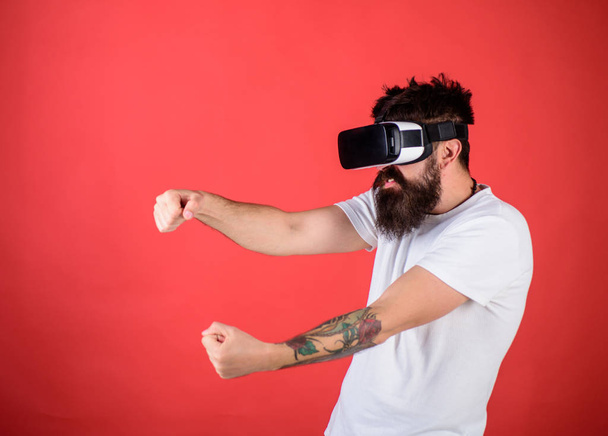 Hombre con barba en gafas VR conduciendo coche, fondo rojo. Concepto de carreras virtual. Guy jugar juego de carreras en VR. Hipster en la cara agresiva coche de conducción en alta velocidad en la realidad virtual
 - Foto, Imagen