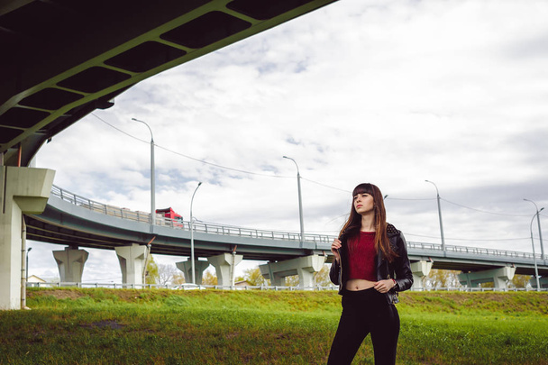 young beautiful stylish woman in fashionable black clothes, a burgundy cardigan and a dark leather jacket posing outdoors near the main road junction - 写真・画像