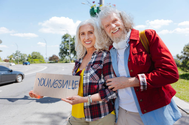 Joyful mood. Aged positive couple standing together at the roadside while looking at you - Photo, Image