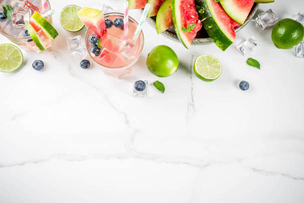 Summer refreshment drink, watermelon and blueberry lemonade cocktail with lime, mint and ice cubes, white marble background copy space top view - Фото, изображение