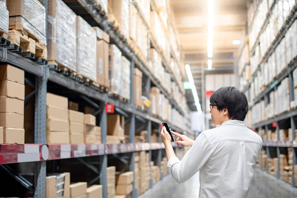 Young Asian man checking the shopping list on his smartphone between product shelves. warehouse shopping lifestyle concept - Photo, Image