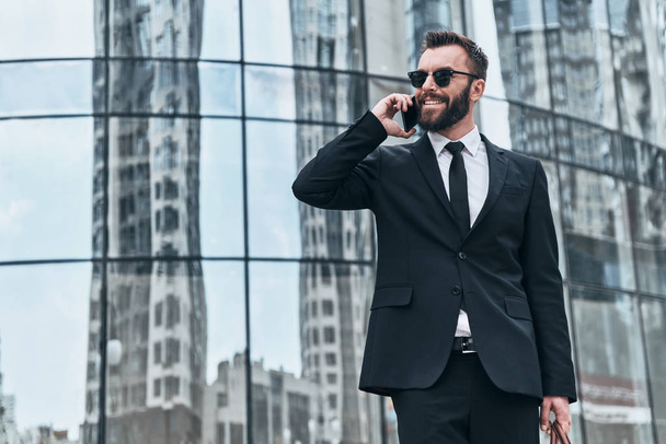 smiling businessman in full suit talking on phone at office glass building  - Fotografie, Obrázek