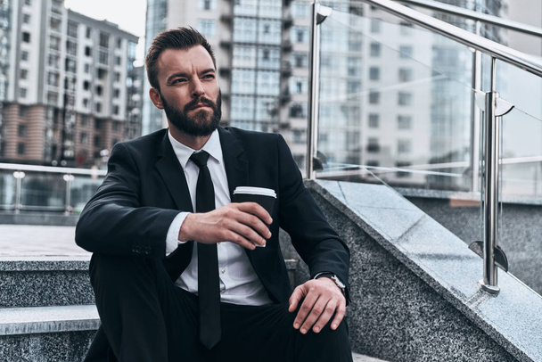 man in suit holding disposable cup and sitting on stairs in street  - Foto, Imagem