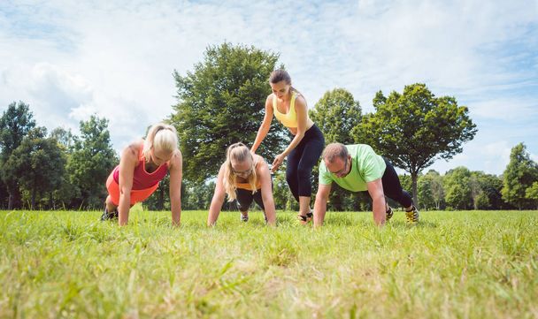 Family doing push-ups in nature under guidance by a fitness coach - Фото, зображення