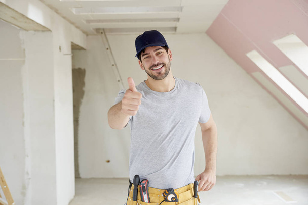 Portrait of young handyman giving thumbs up while standing at construction site.  - Photo, Image