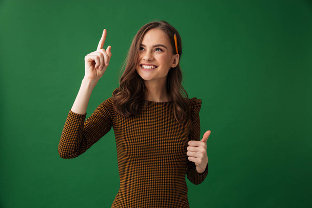Image of cheerful young woman standing isolated over green background pointing make thumbs up. - Фото, изображение