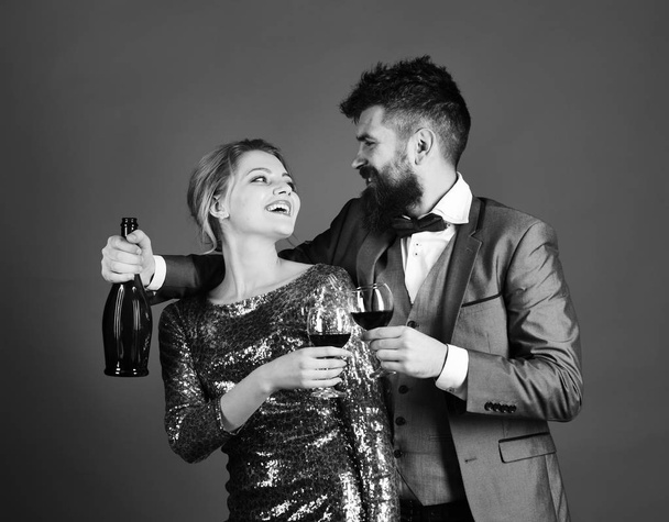 Lady and gentleman celebrating with merlot wine. Woman in sparkling dress and man holding bottle of wine - Fotó, kép